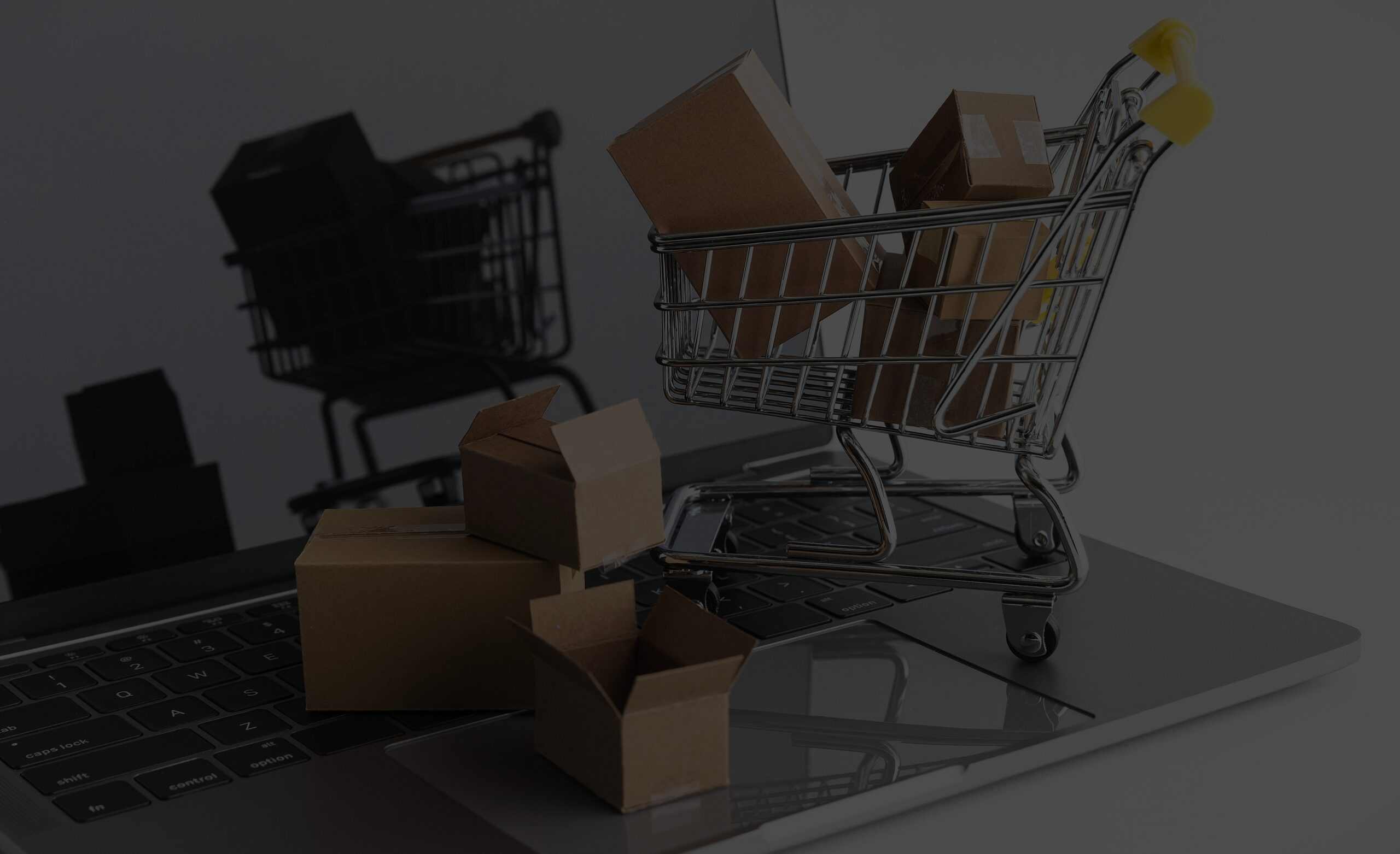 Chariot de supermarché rempli de boîtes sur un ordinateur portable, symbolisant le commerce électronique. -KIOMA Meuble Premium Maroc